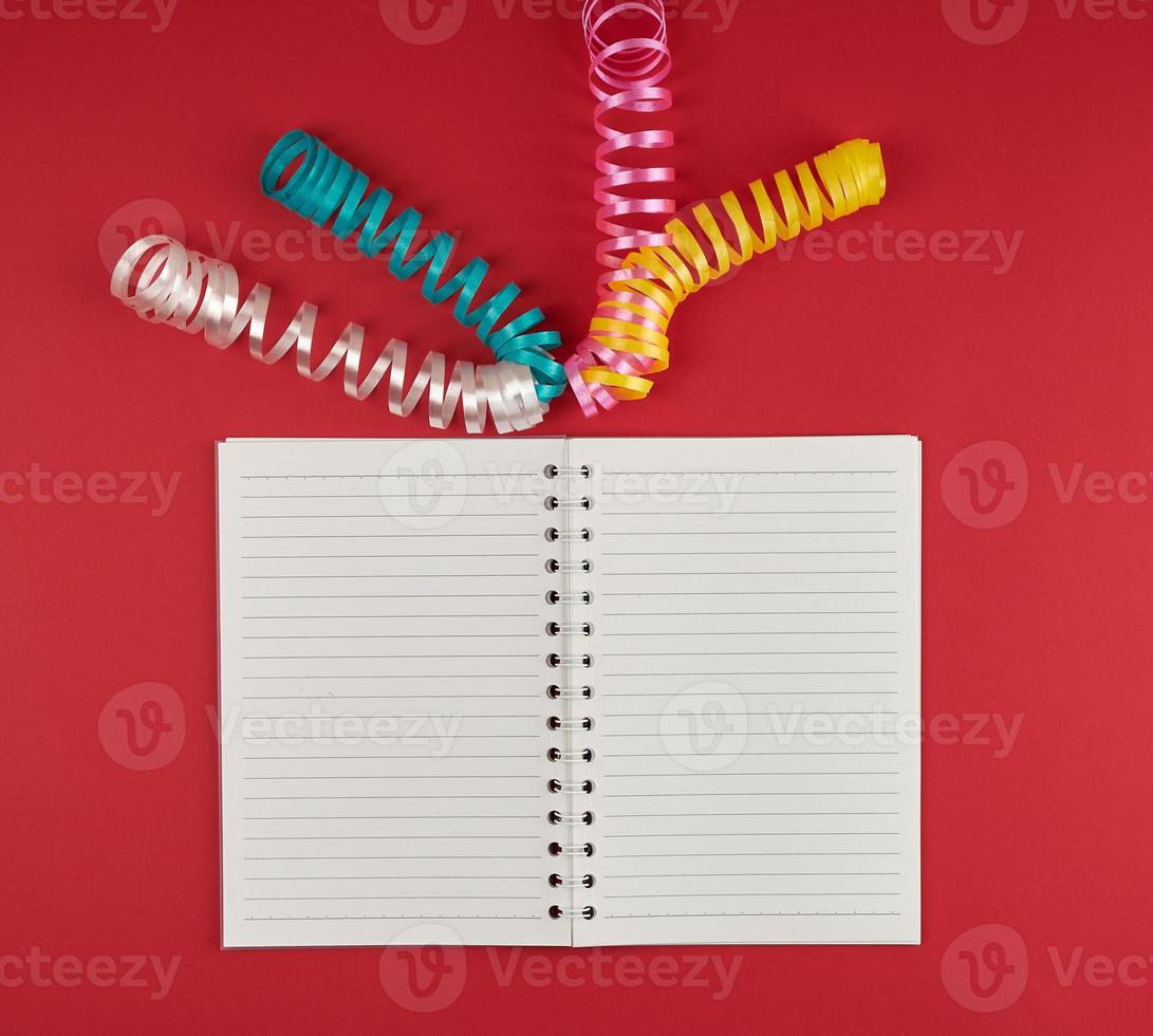 open notebook in line and multicolored serpentine on a red background photo