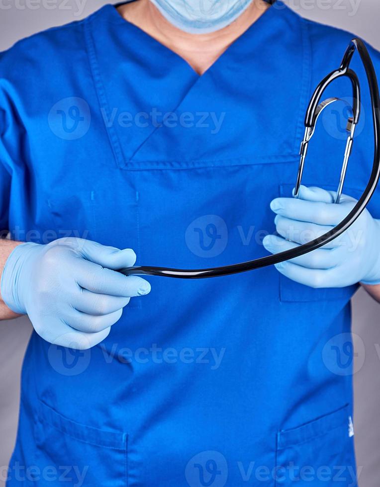 doctor in blue uniform and latex gloves holding a black stethoscope photo
