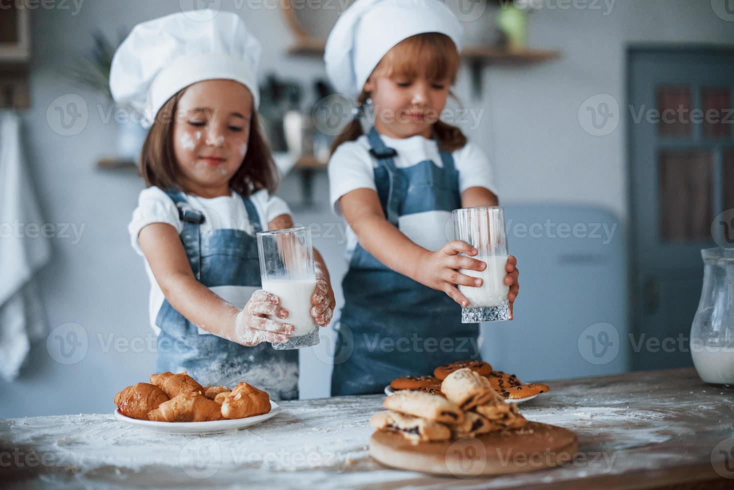 Wth glasses with milk. Family kids in white chef uniform preparing food on the kitchen photo