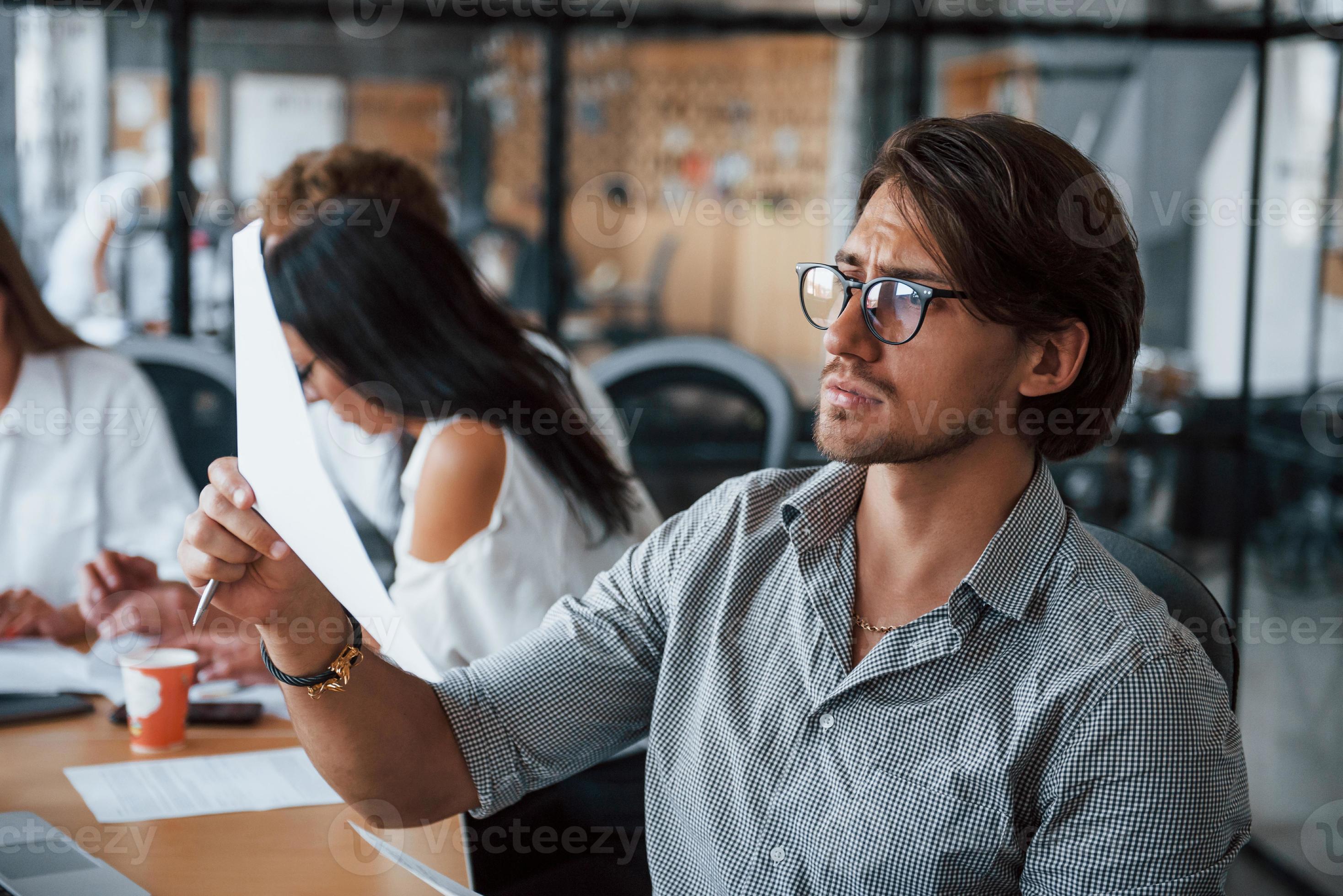 Guy in glasses in front of his employees. Young business people in formal clothes working in the