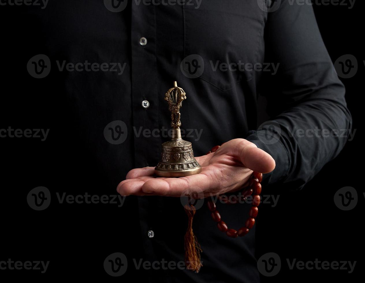 un hombre adulto con una camisa negra sostiene una campana ritual tibetana de cobre, de bajo perfil foto