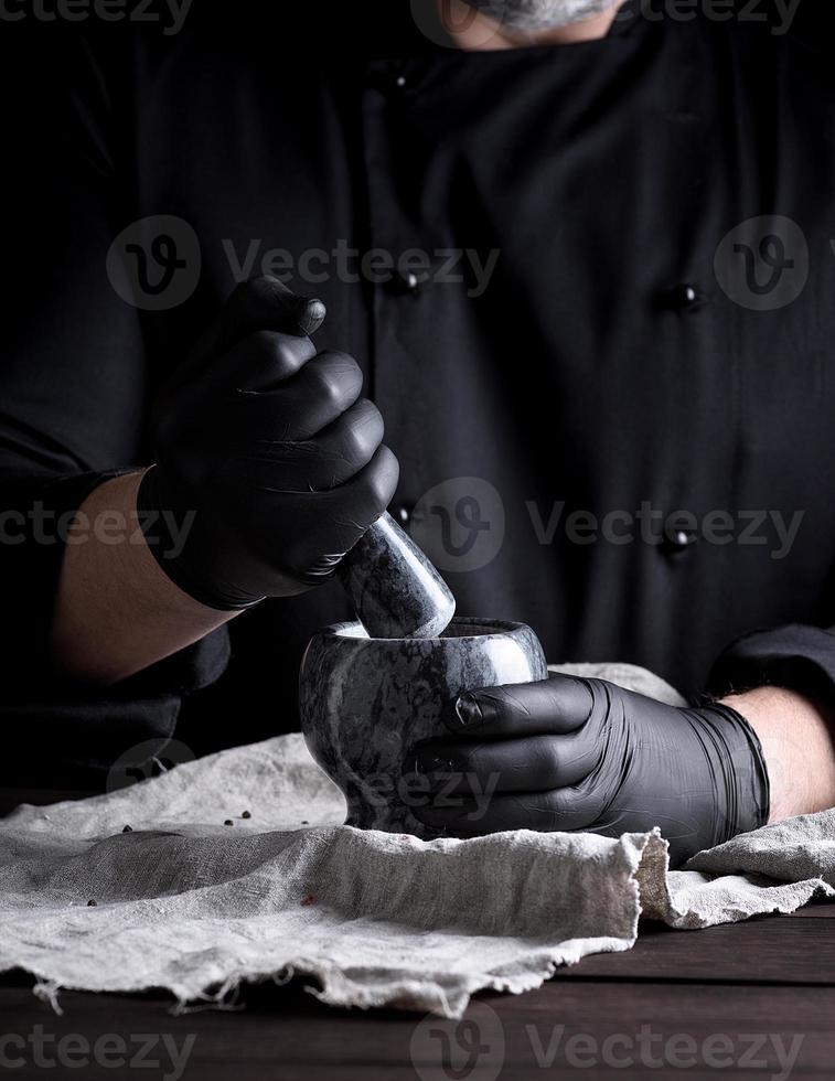 cook in black latex gloves holding a stone mortar with pepper photo