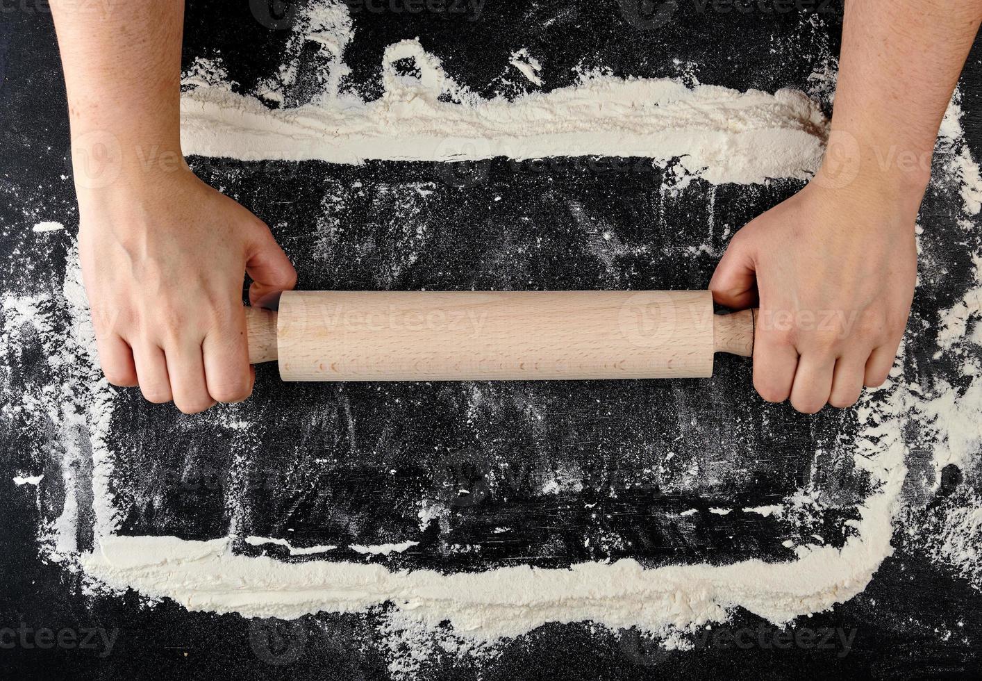 wooden rolling pin in female hands on a black background with white wheat flour photo