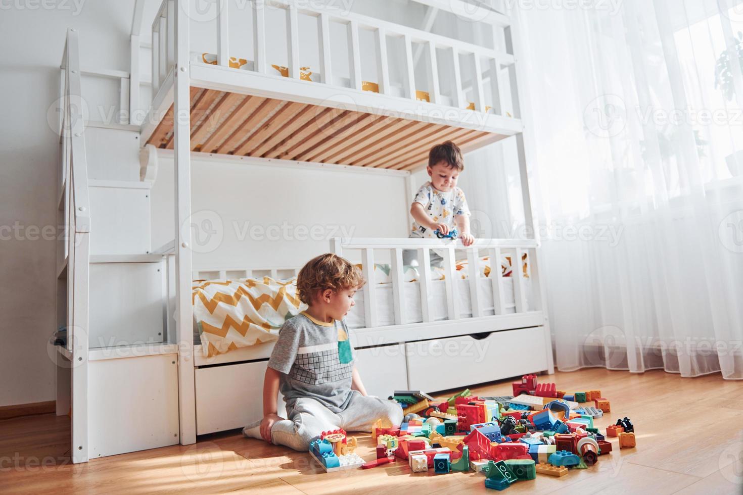 Two little boys have fun indoors in the bedroom with plastic construction set photo