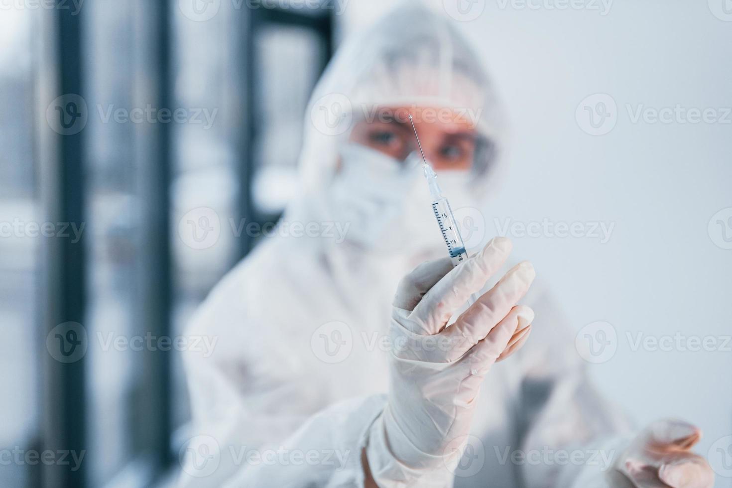 sostiene la jeringa. retrato de una doctora científica con bata de laboratorio, anteojos defensivos y máscara foto