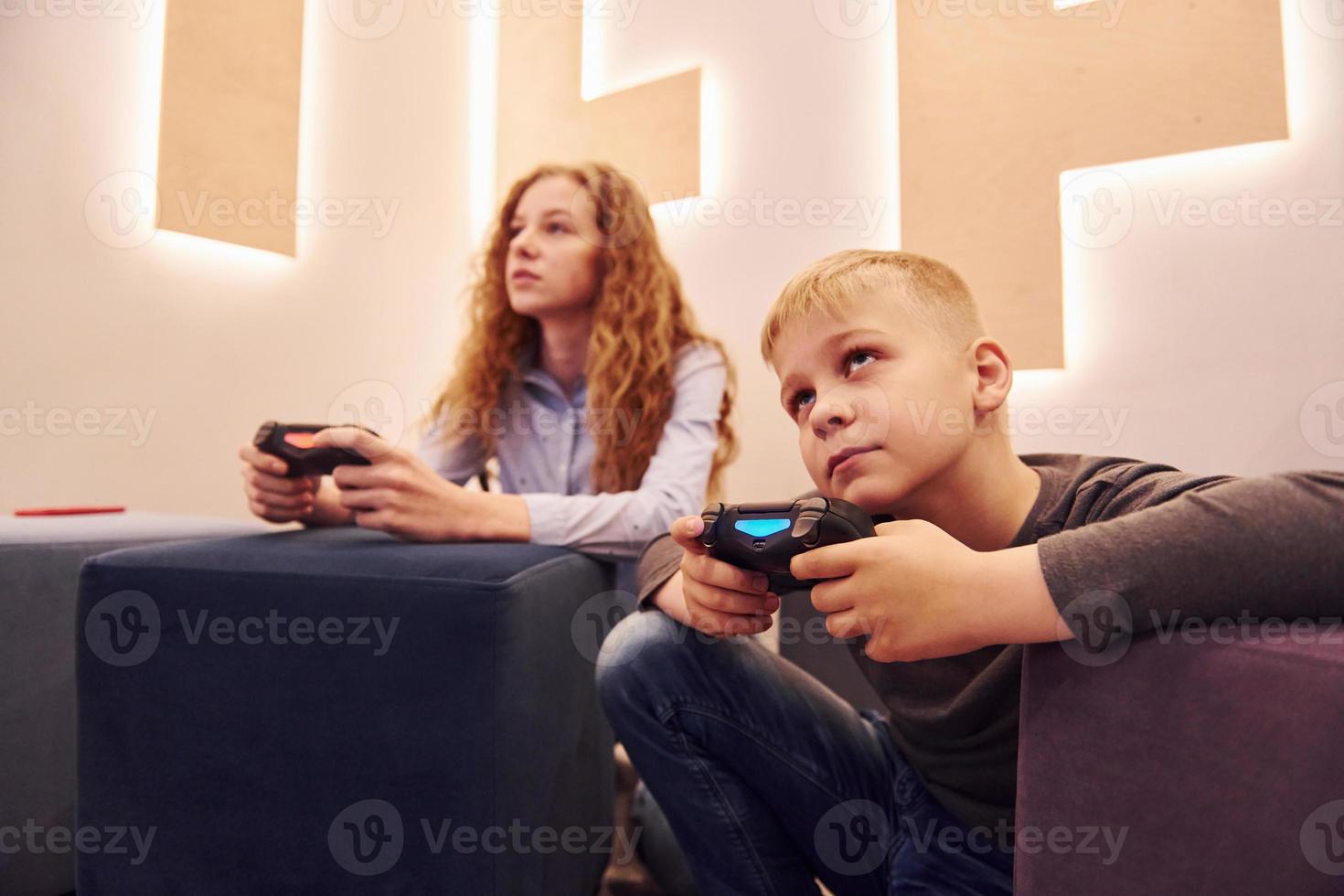 niños alegres sentados adentro y jugando videojuegos juntos foto