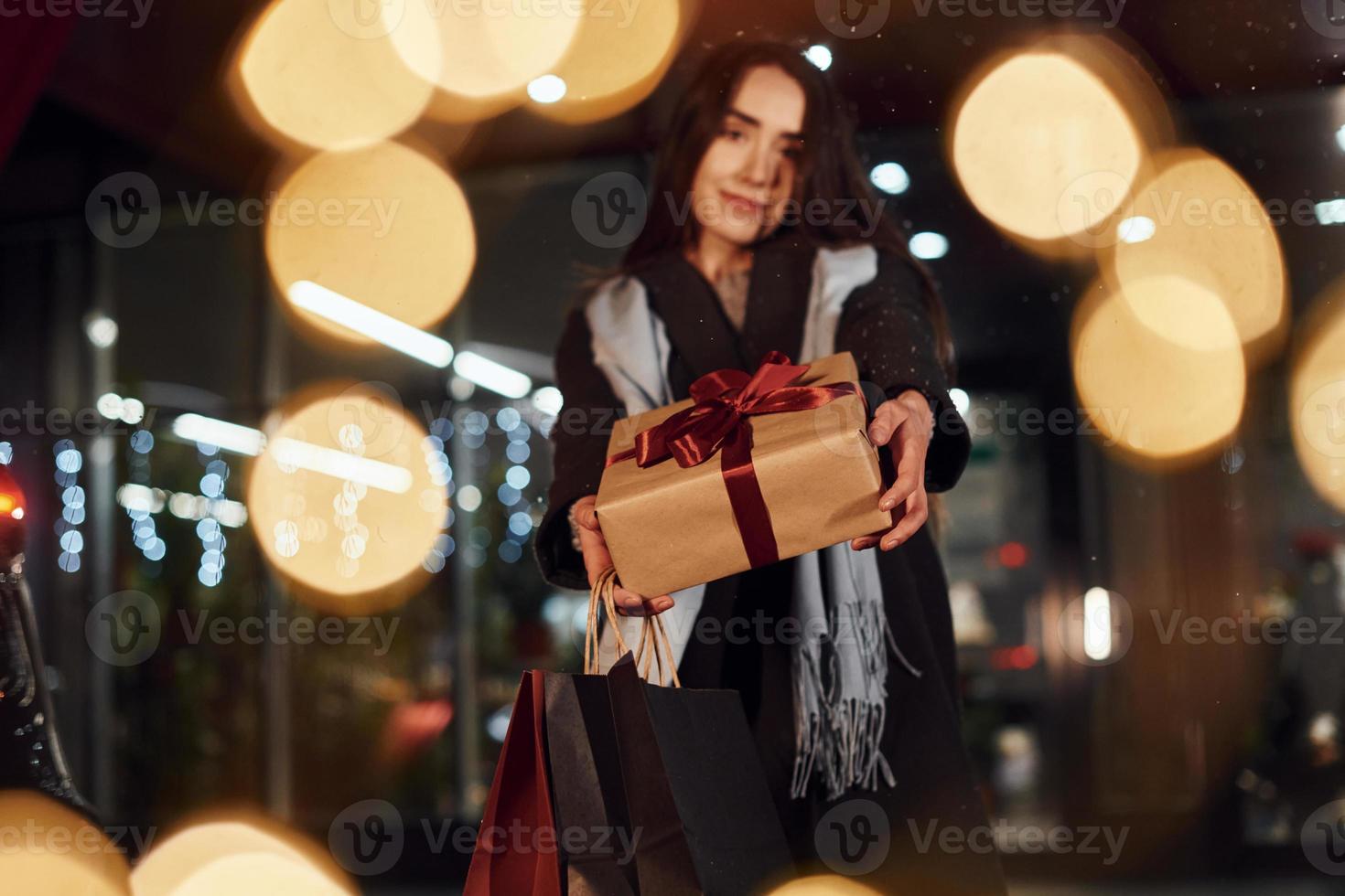 From the shop with gift box in hands. Cheerful woman is outdoors at Christmas holidays time. Conception of new year photo