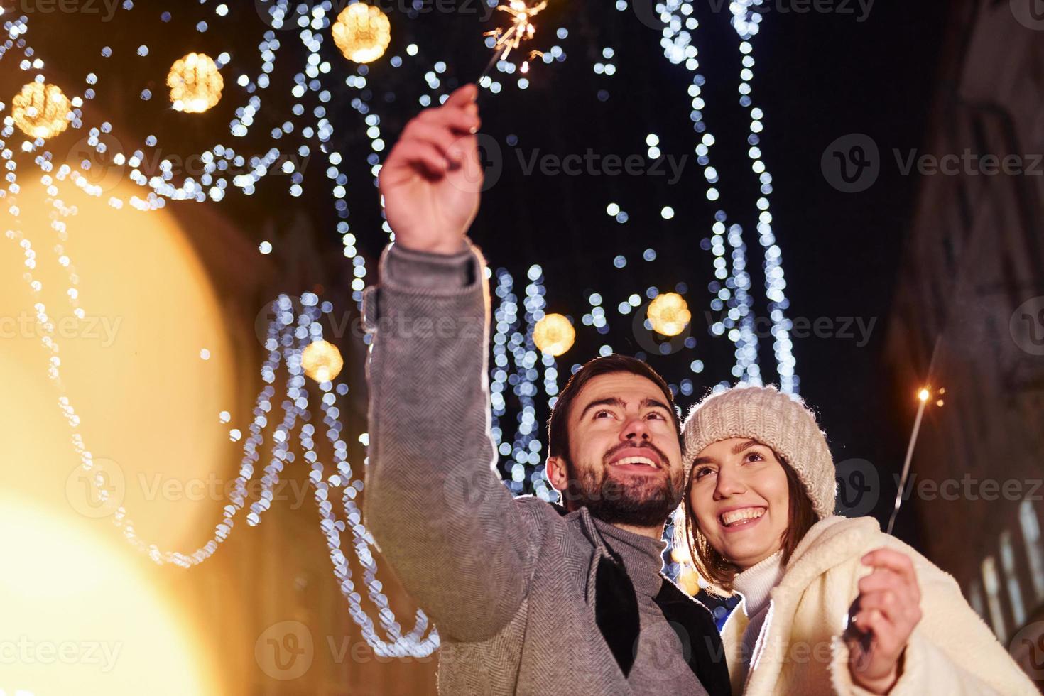 With sparklers in hands. Happy young couple celebrating New year outdoors on the street photo