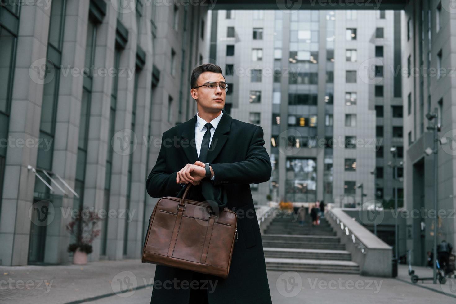 Front view. Businessman in black suit and tie is outdoors in the city photo