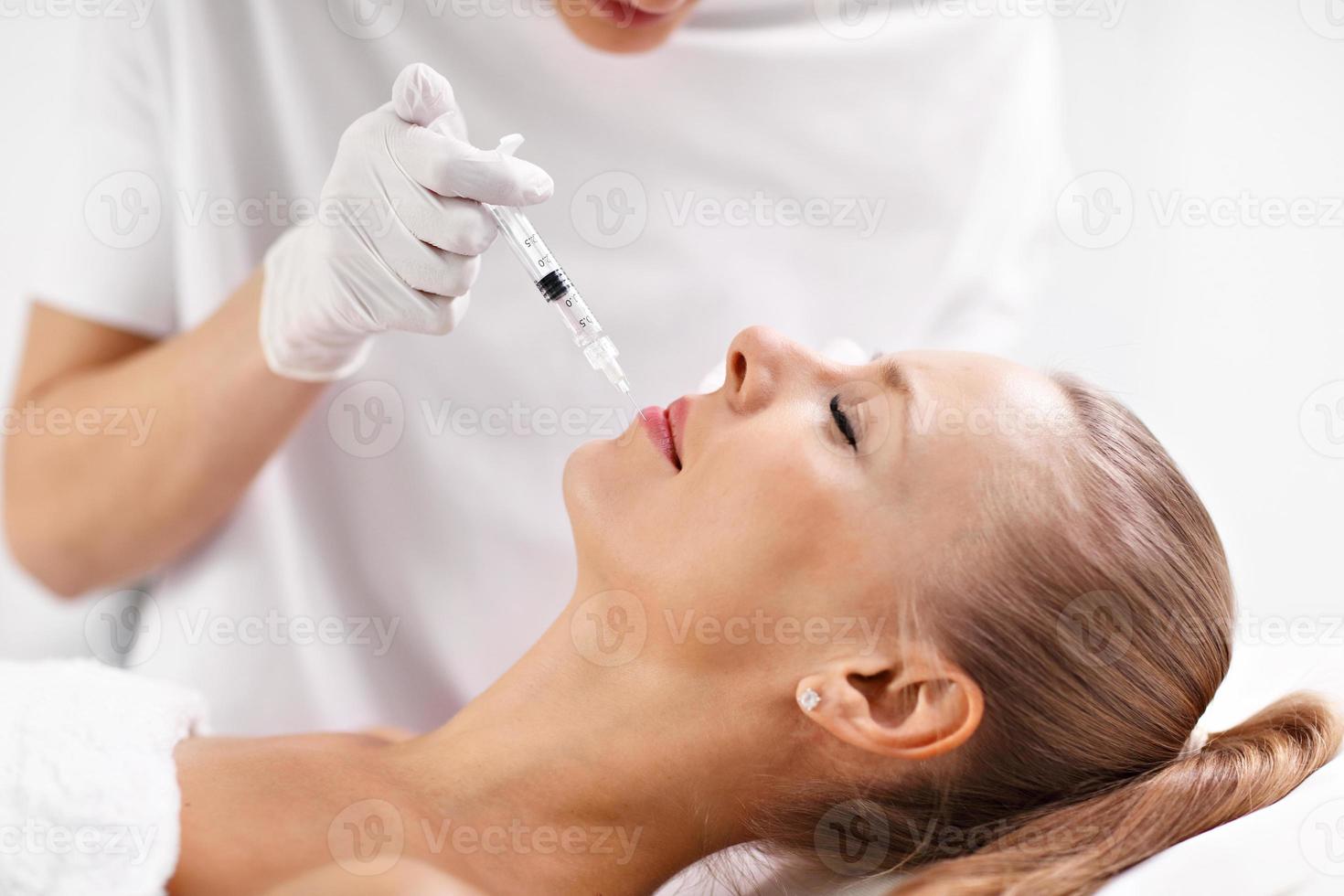 Close up of hands of cosmetologist making botox injection in female lips photo