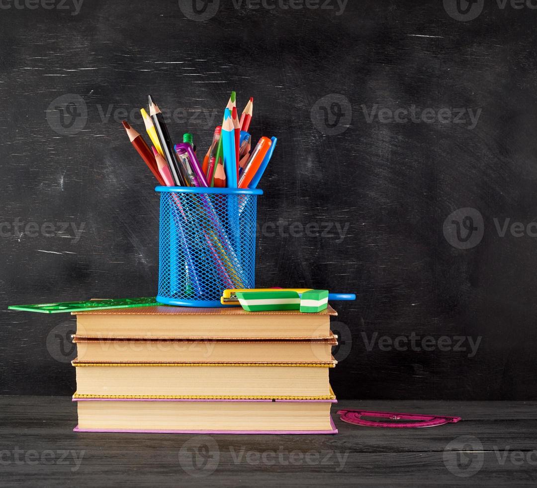 pila de libros y un vaso de papelería azul con lápices de madera multicolores foto