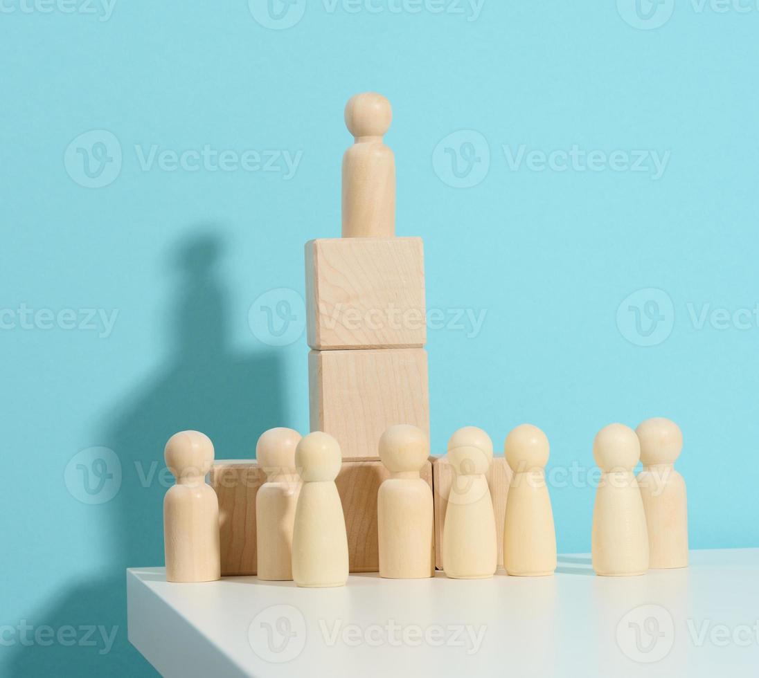 wooden figurine of a man stands on a high podium of cubes, below the crowd. Search for talented employees, rally, manipulation of the masses, selection of employees for the team photo