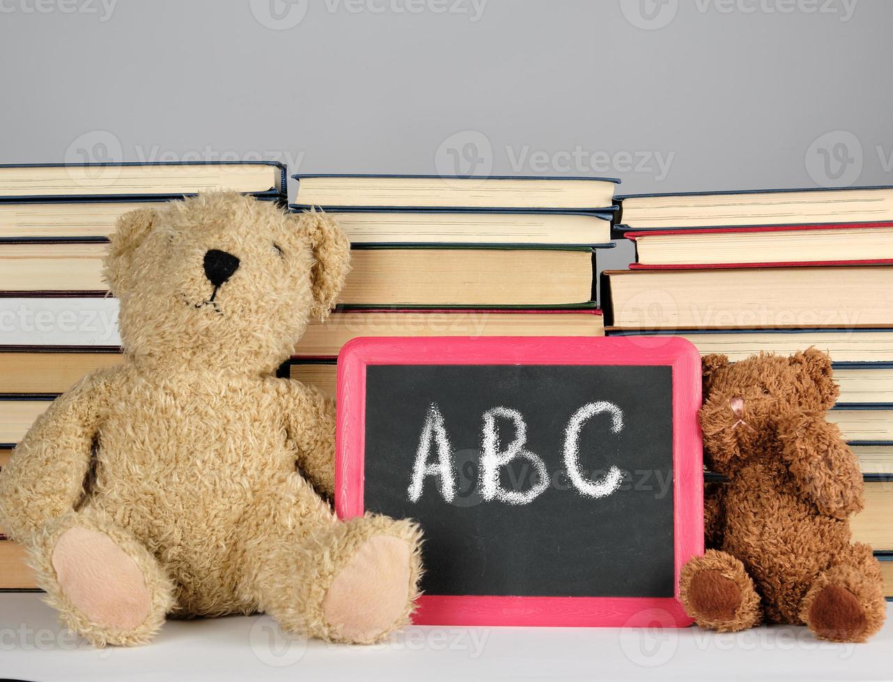 brown teddy bear and empty black board in red frame on the background of pile of books photo