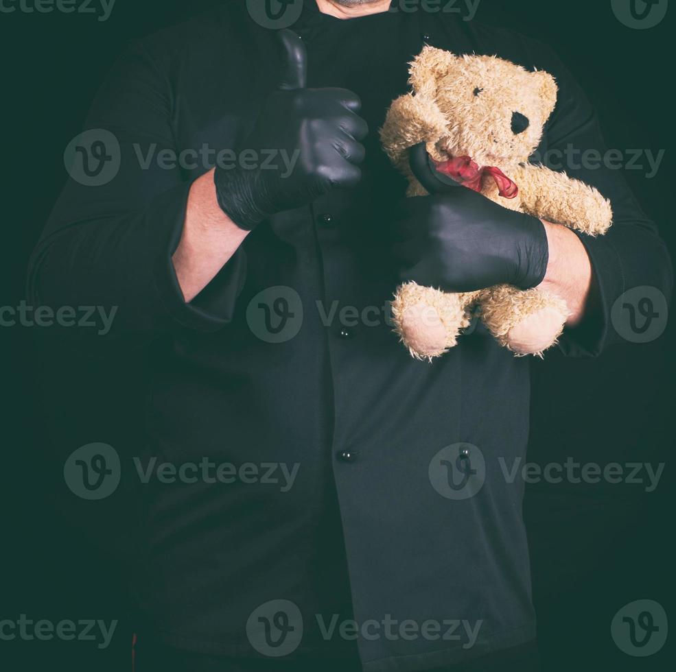 hombre vestido de negro sosteniendo un oso de peluche marrón foto