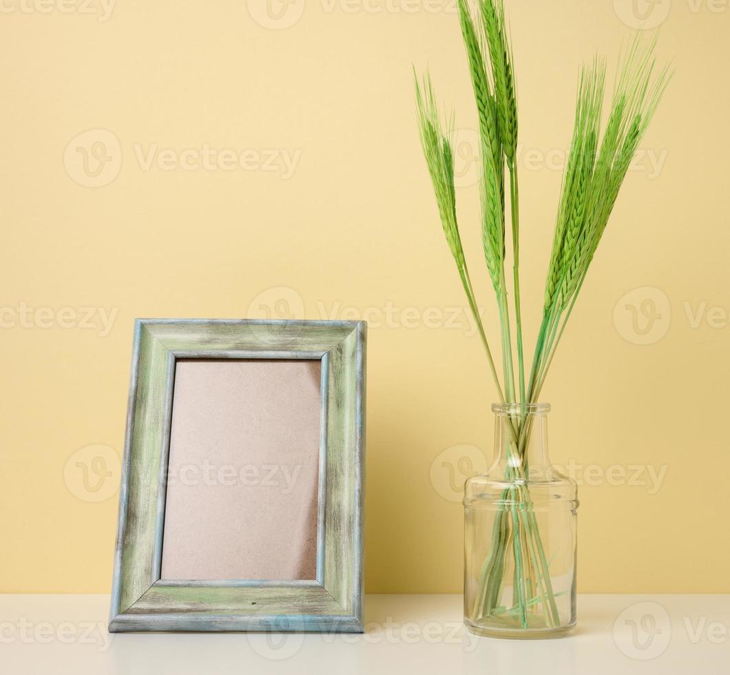 empty white wooden photo frame and green plants on white table, yellow background