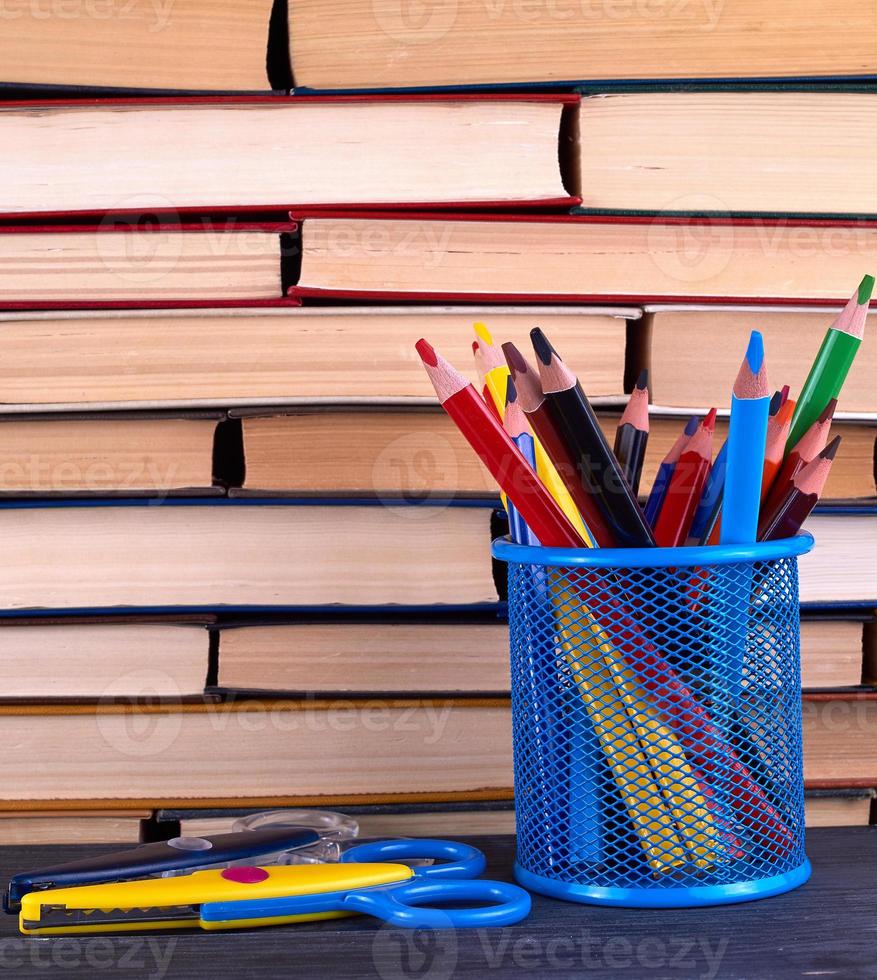 stacks of various hardback books and blue stationery glass with multi-colored wooden pencils photo