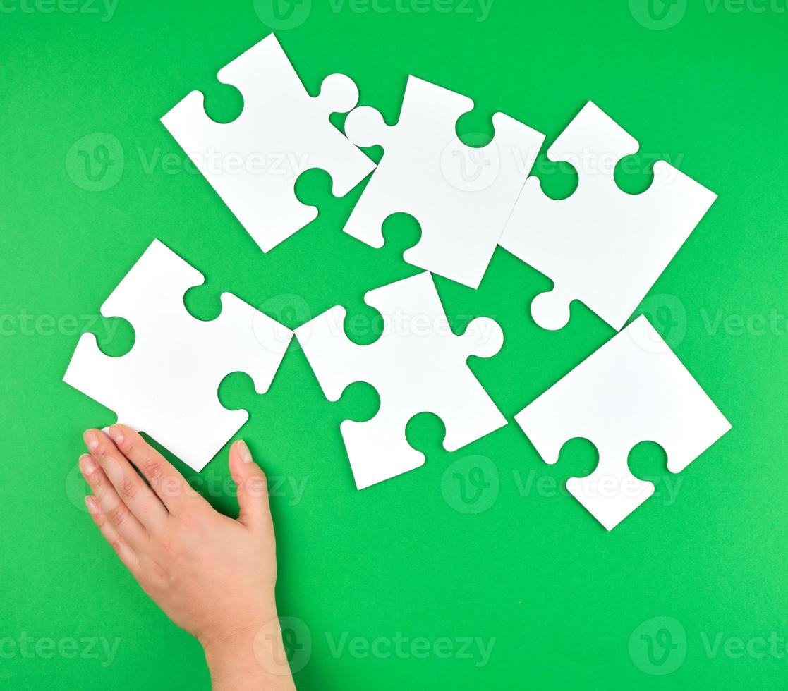 female hand puts empty white big puzzles on a green background photo