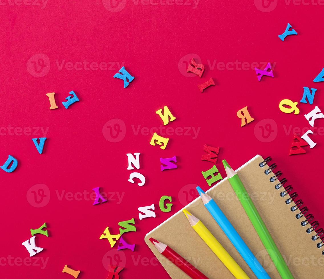 notebook and multicolored wooden pencils on a red background photo