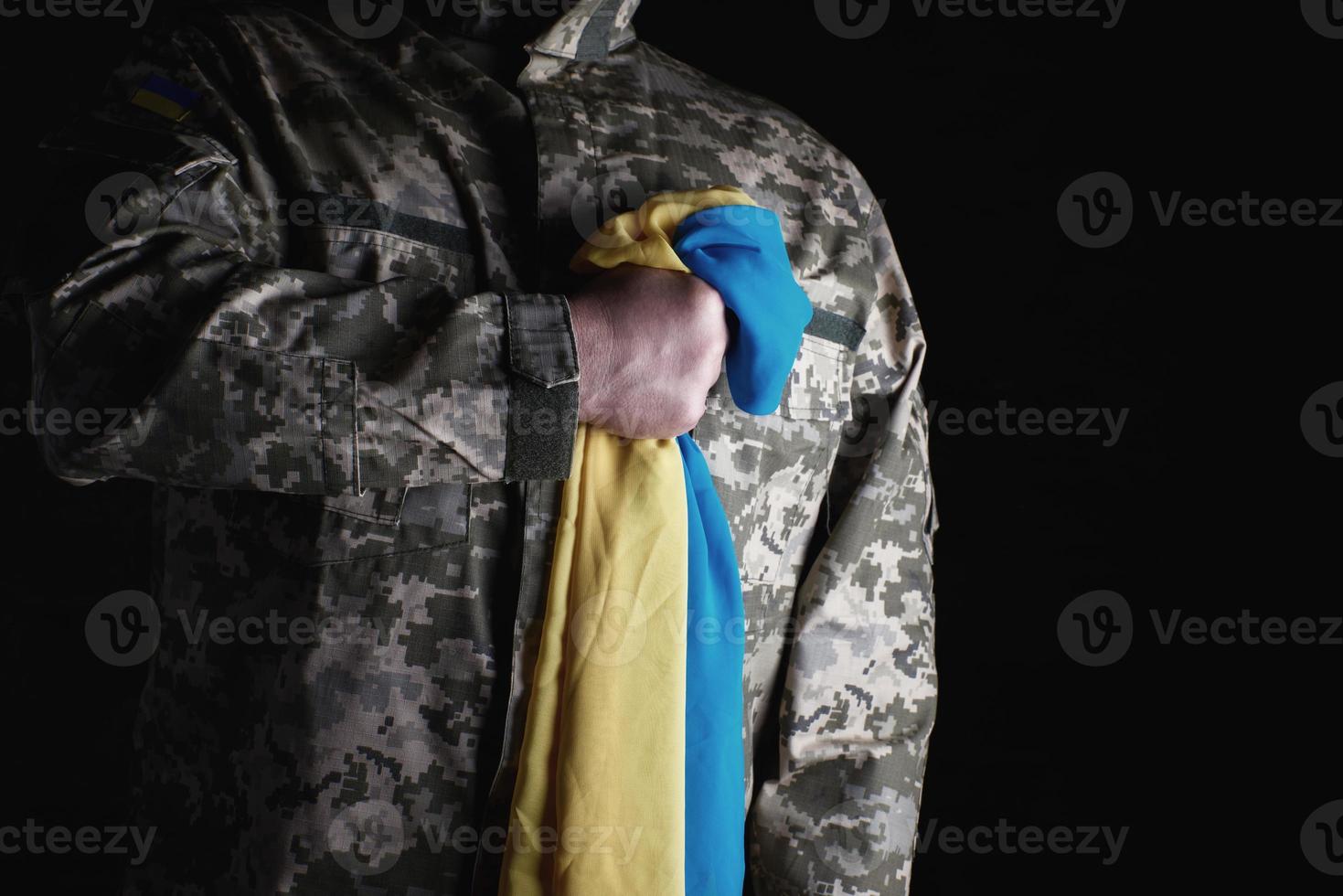 Ukrainian soldier holds in his hand the yellow-blue flag of the state, he pressed his hand to his chest photo