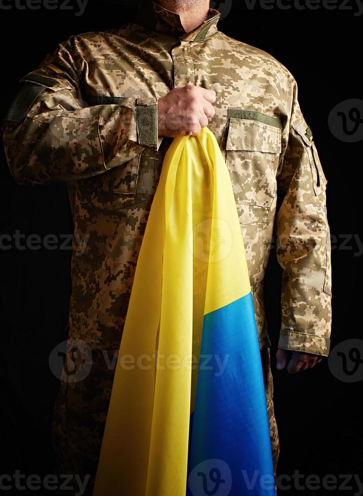 soldado ucraniano sostiene en su mano la bandera amarilla-azul del estado foto