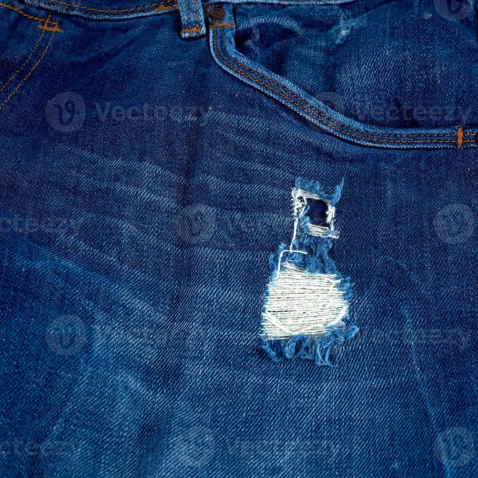 fragment of blue jeans fabric with a hole photo