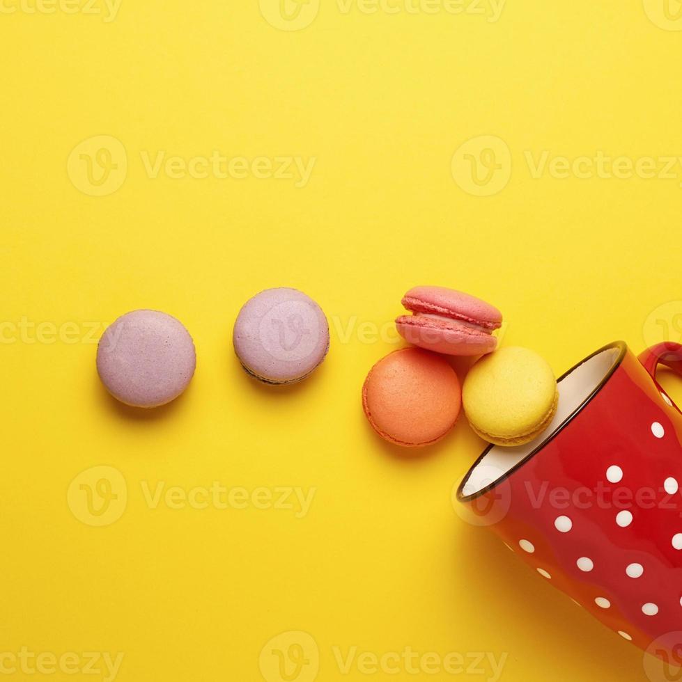 round multicolored macarons falling from a red ceramic cup with polka dots photo