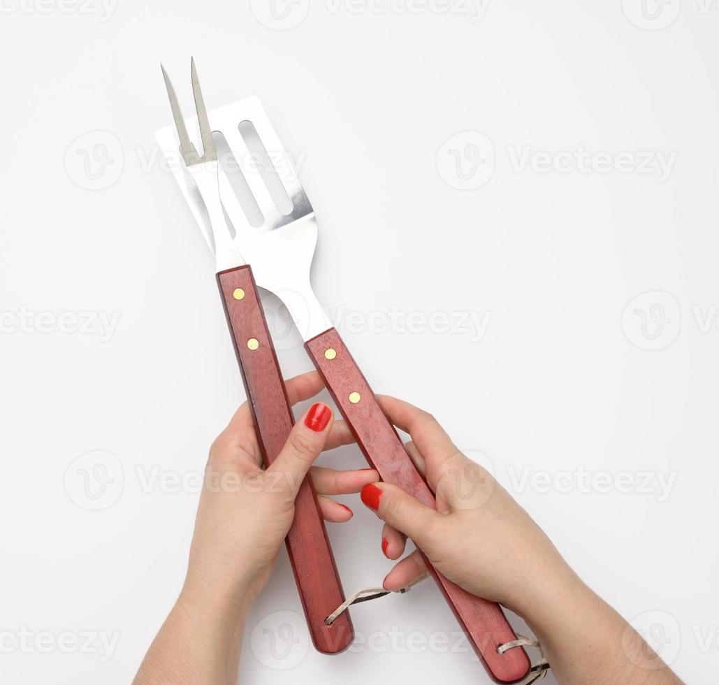 metal spatula with a wooden handle and fork for a picnic in a female hand with painted red nails on a white background photo