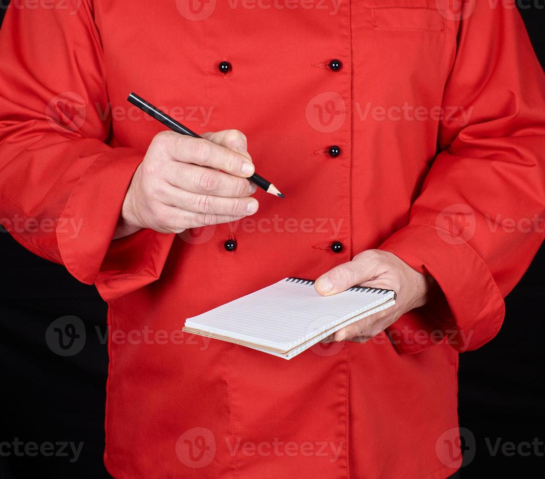 chef con uniforme rojo sosteniendo un cuaderno en blanco y un lápiz de madera negro foto