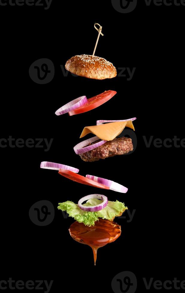 Flying ingredients of a classic cheeseburger sesame bun, onion rings, tomato slices and a juicy barbecue cutlet photo
