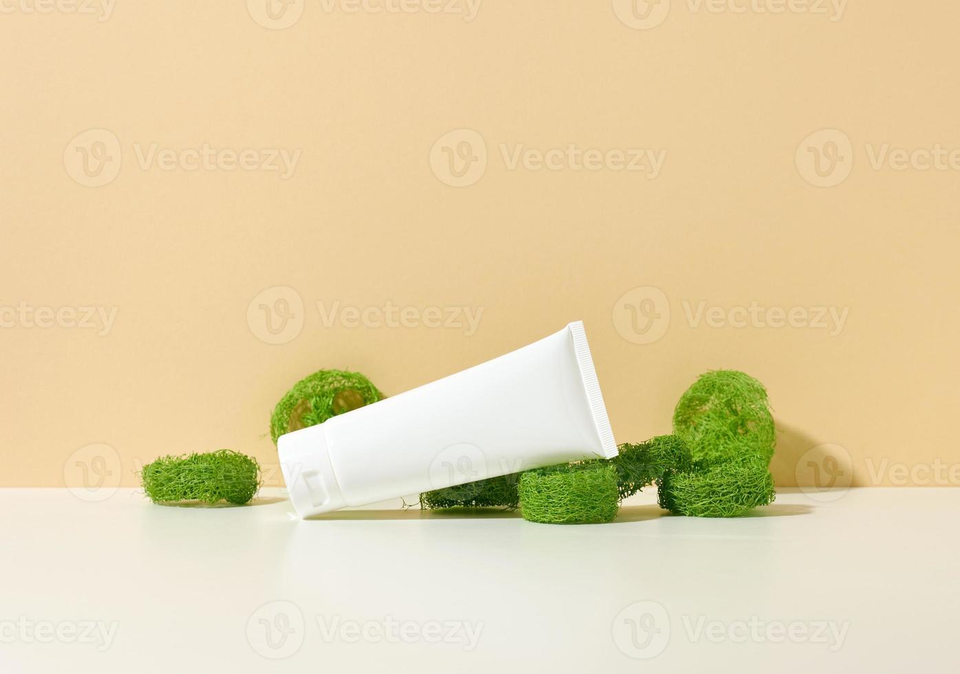 empty white plastic tube on a beige background and pieces of green loofah. Cosmetic products for branding gel, cream, lotion, shampoo. photo