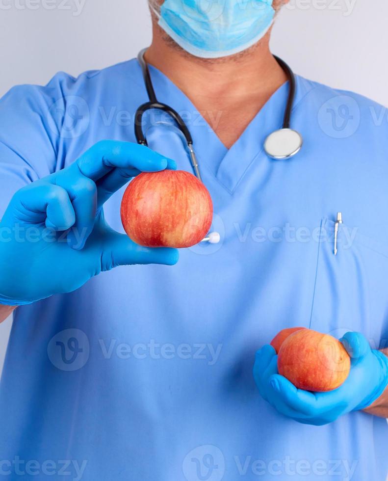 doctor in blue uniform and sterile latex gloves holds ripe red apples photo