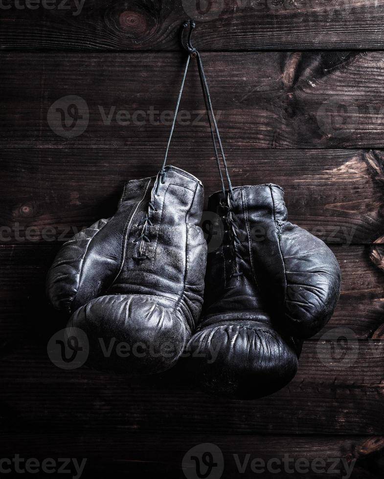 pair of very old shabby black leather boxing gloves hanging on a nail photo