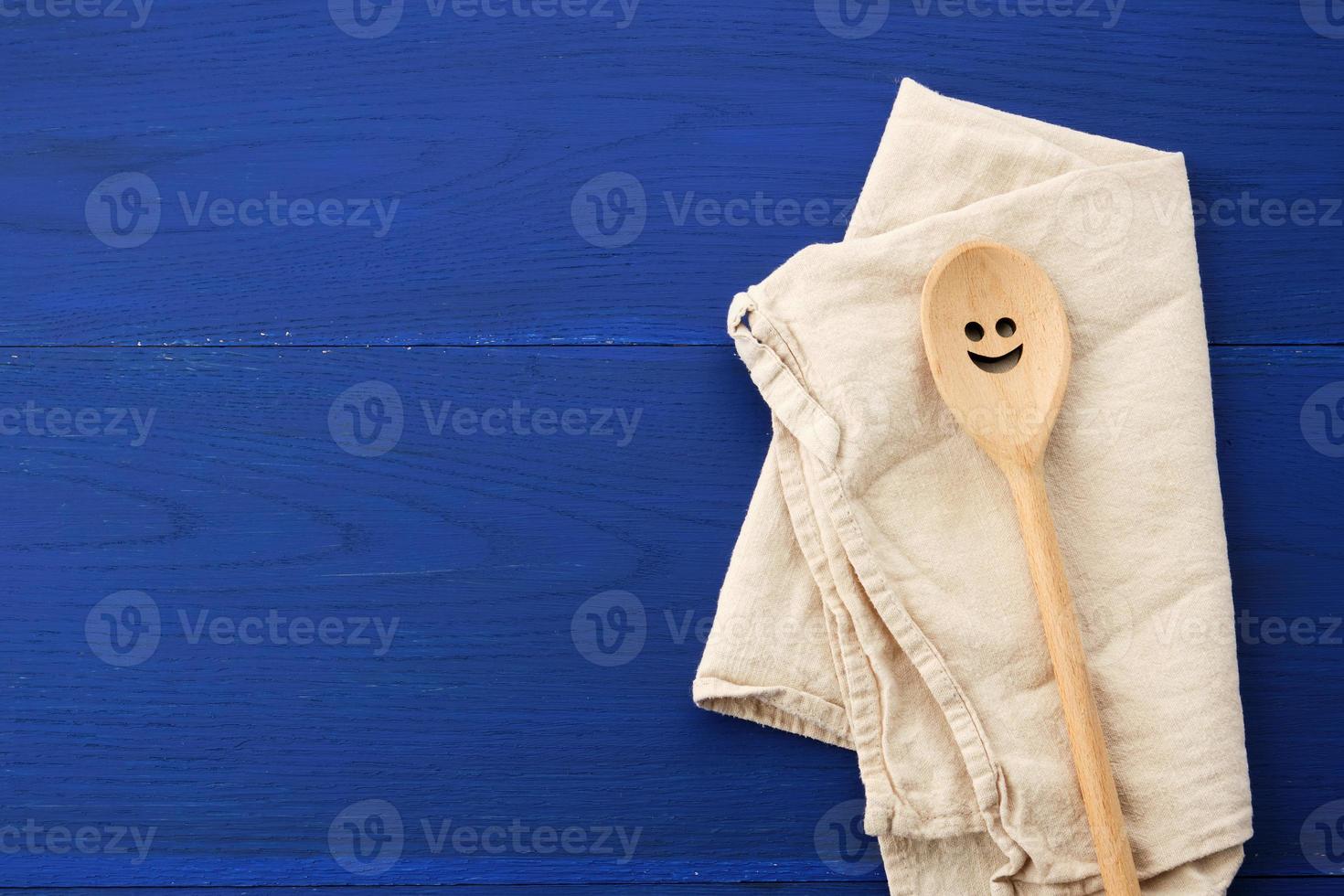 vintage wooden spoon and white textile kitchen towel on blue wooden background photo