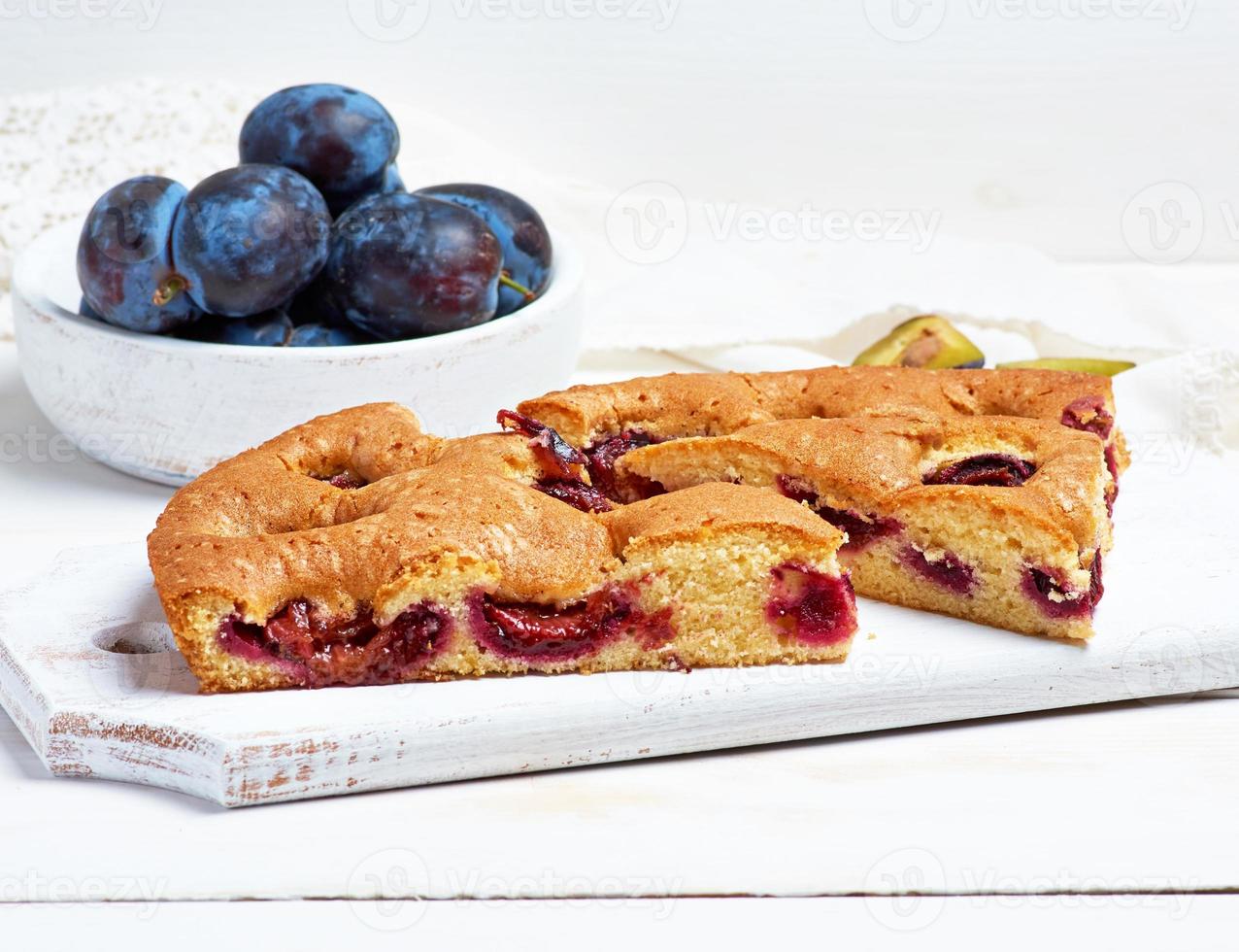 slices of biscuit plum cake on a white wooden board and fresh fruits photo