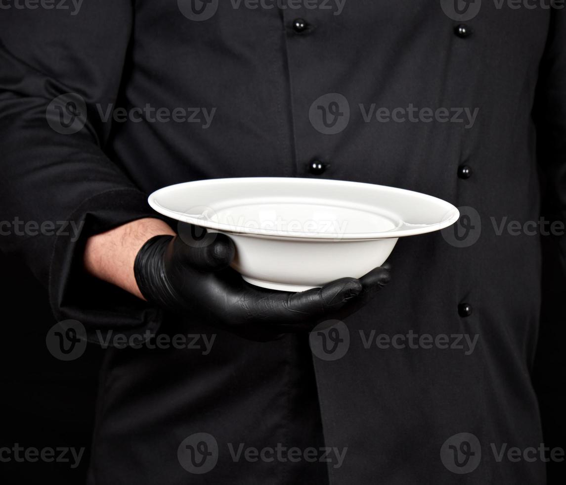 cocinero con uniforme negro y guantes de látex negros sostiene en su mano un plato blanco redondo y vacío foto