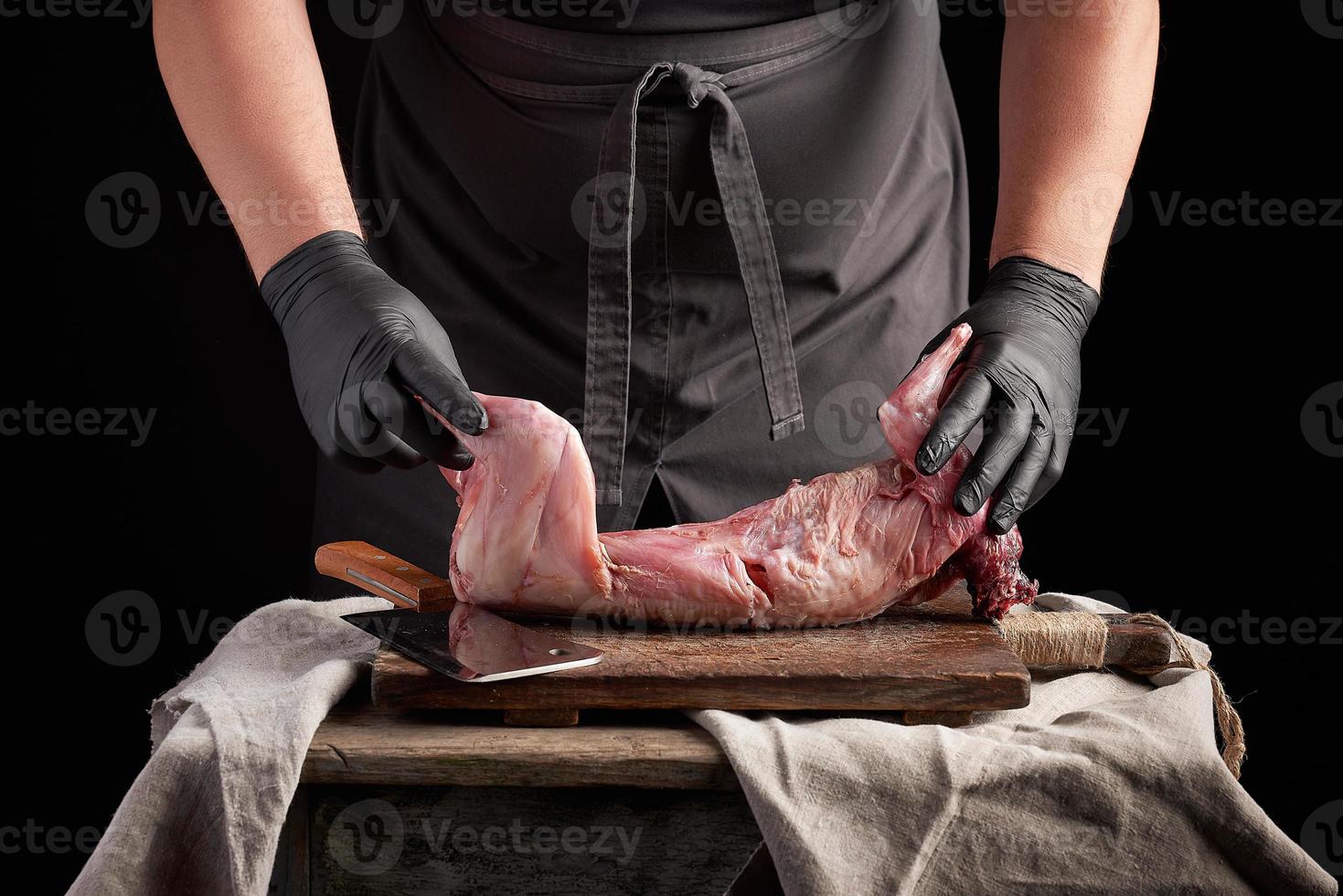 chef in black latex gloves holds a whole rabbit carcass on a brown cutting board photo