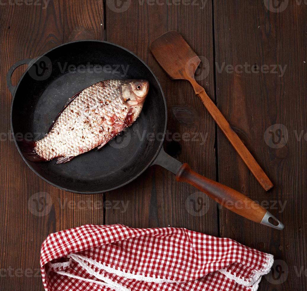 fresh crucian fish sprinkled with spices and lies in a black round pan photo