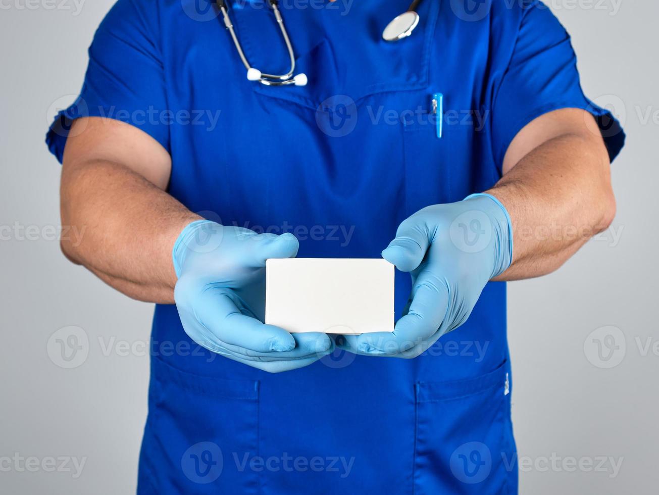 doctor in sterile latex gloves and blue uniform holds a blank white business card photo