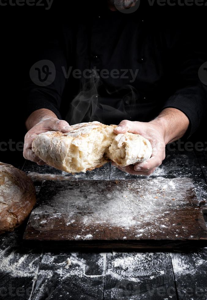 male hands breaking open baked bread in half over black wooden table photo