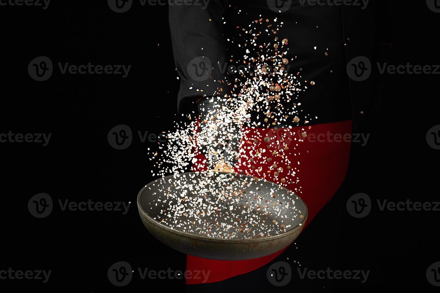 chef holds a round pan and throws the mixture of spices and white salt up photo