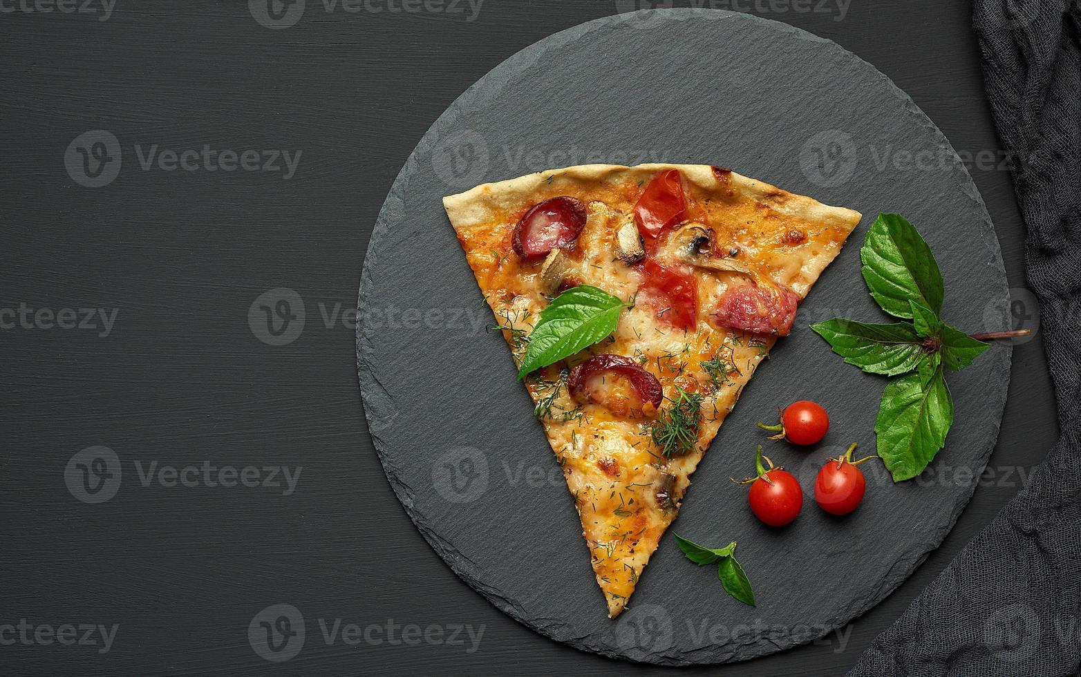 delicious triangular slice of pizza with smoked sausages, mushrooms, tomatoes, cheese and basil leaves photo