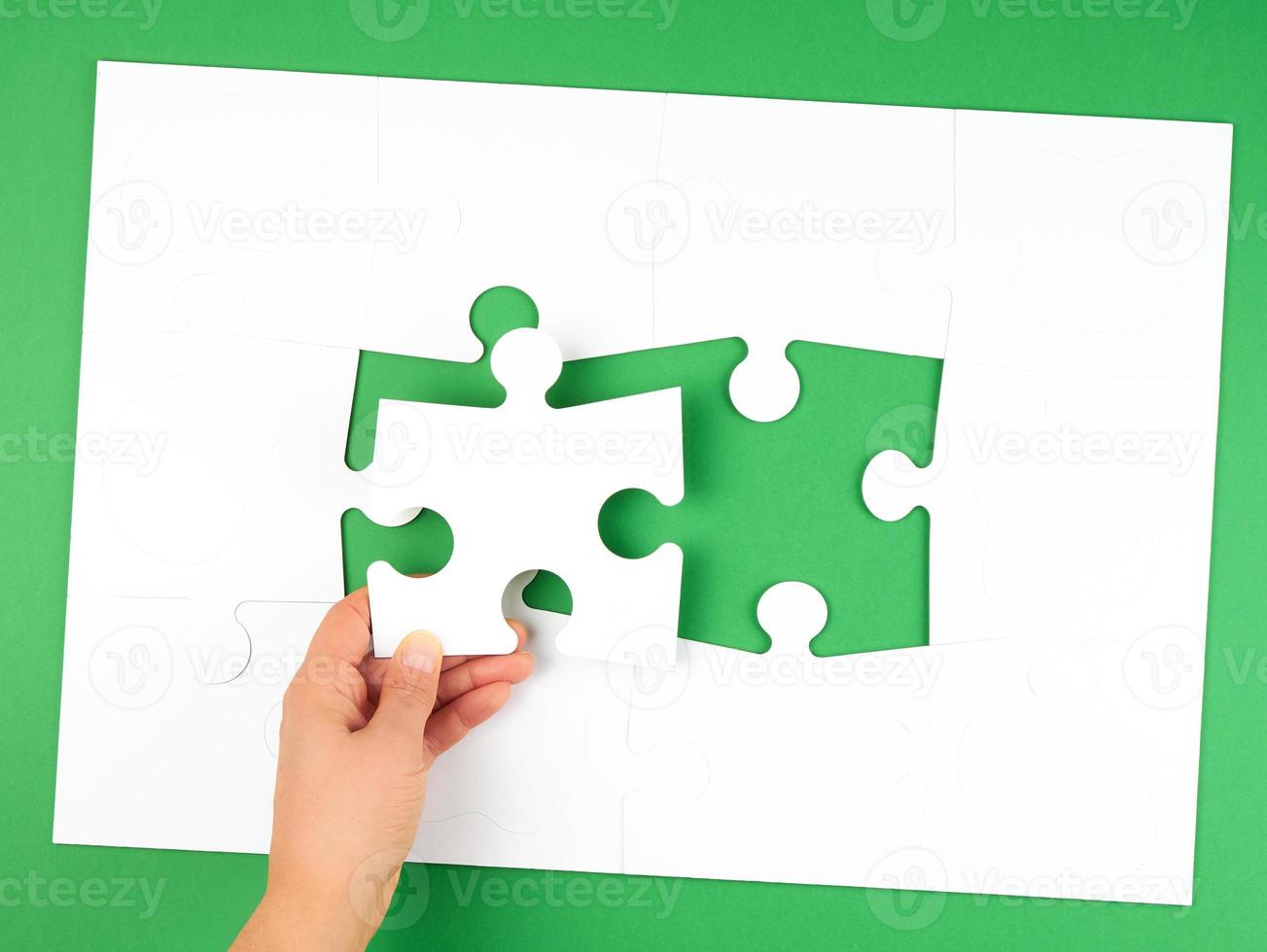 female hand puts empty white big puzzles on a green background photo