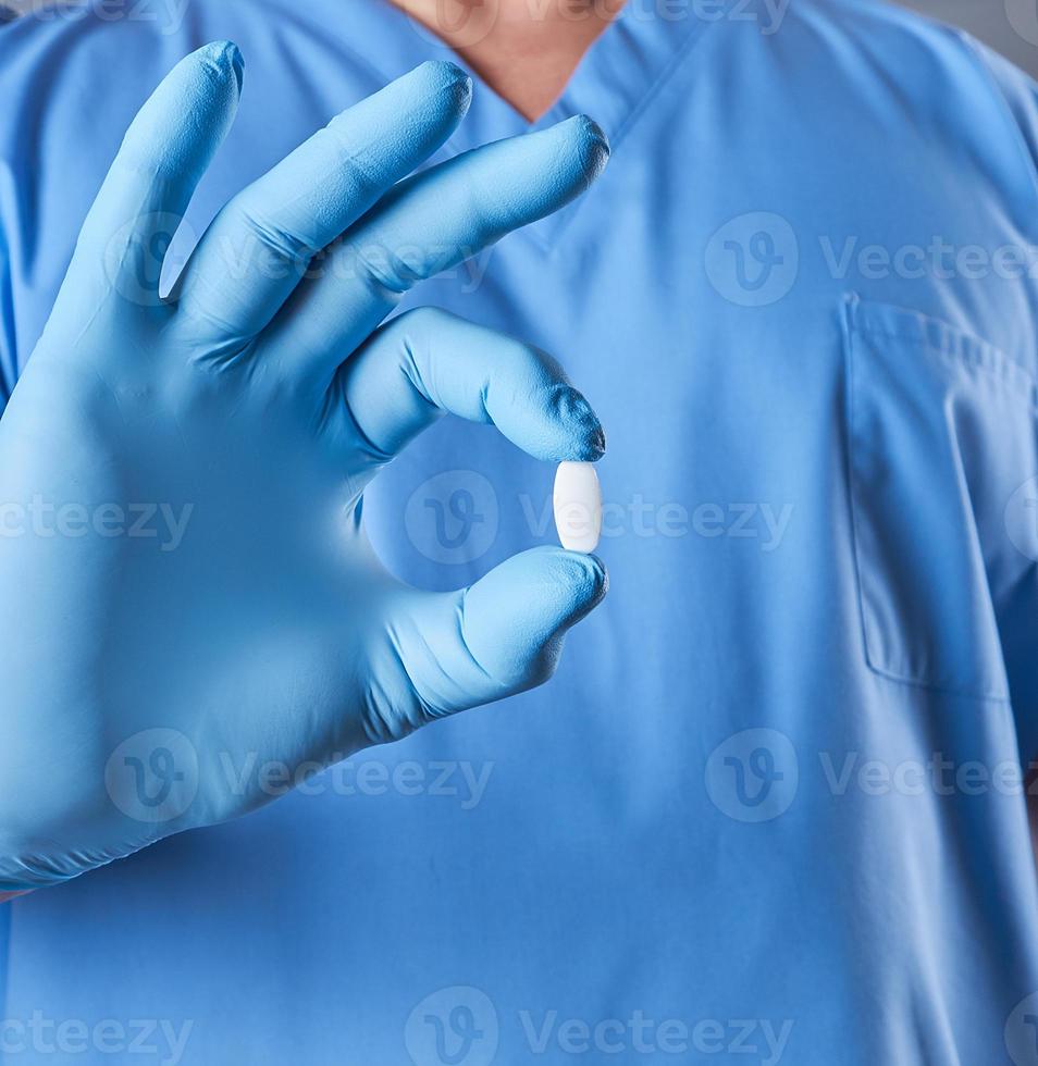 médico con guantes de látex azules sosteniendo una pastilla blanca foto