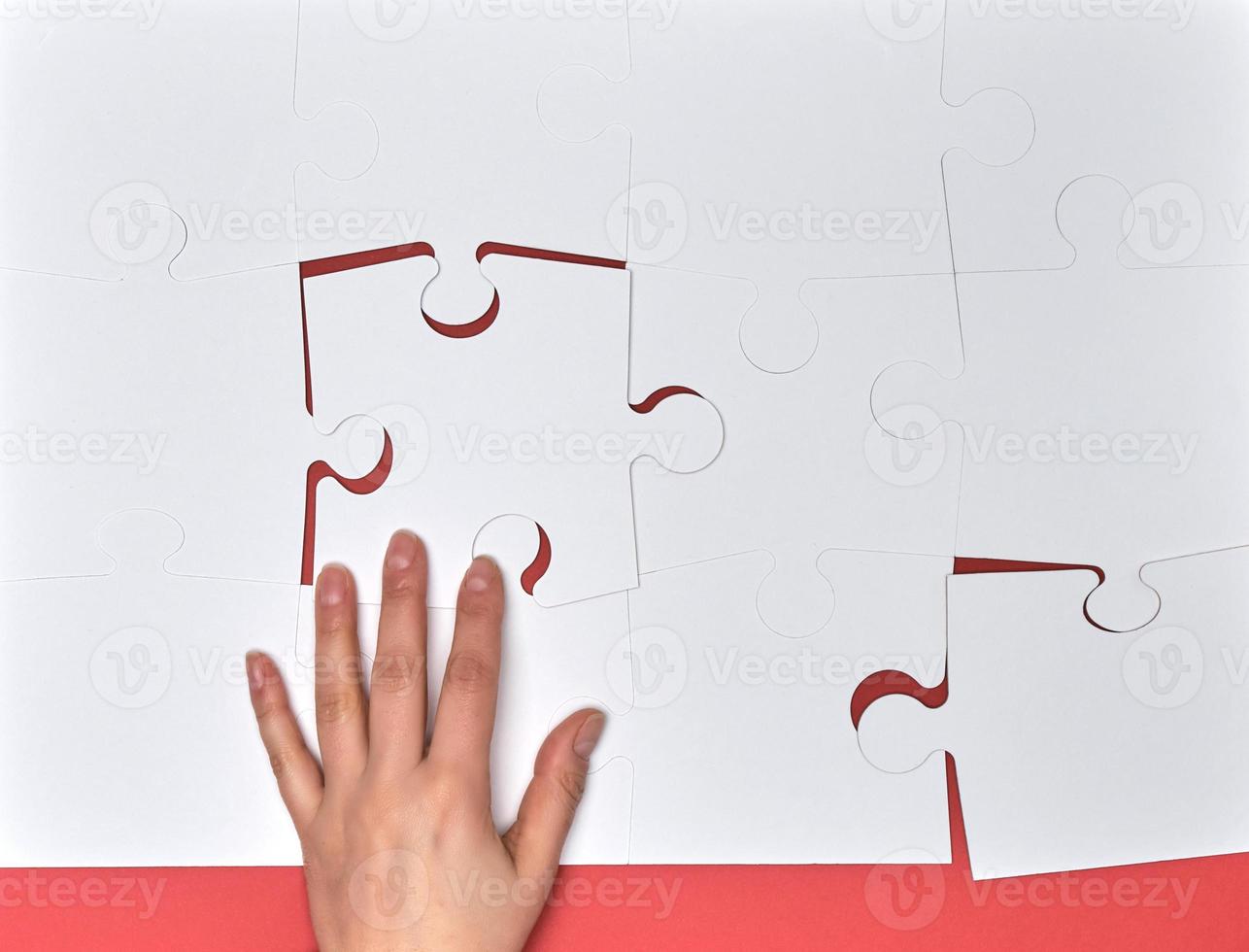 female hand puts white big puzzles on a pink background photo