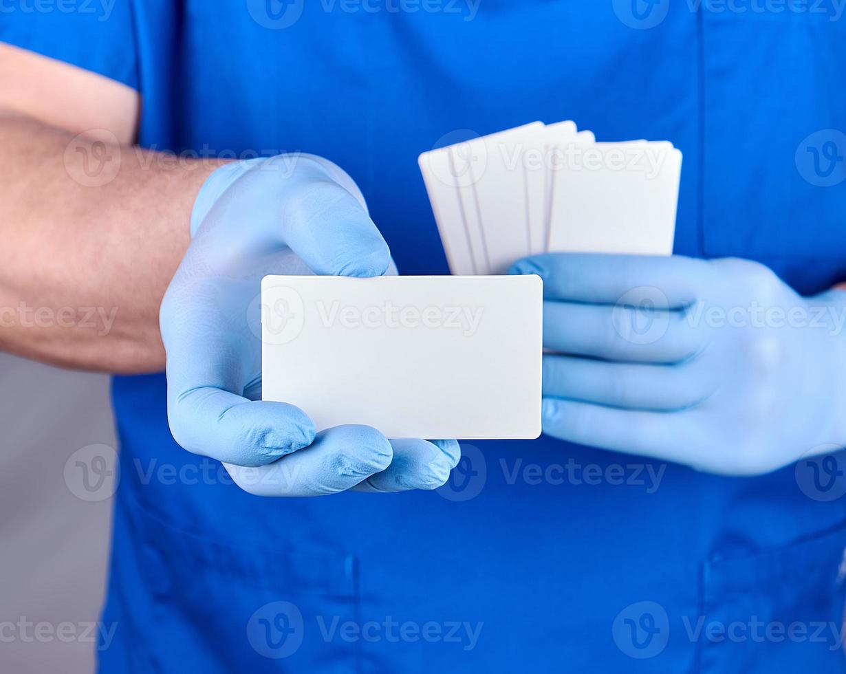 male doctor wearing blue latex gloves is holding a blank white paper business card photo