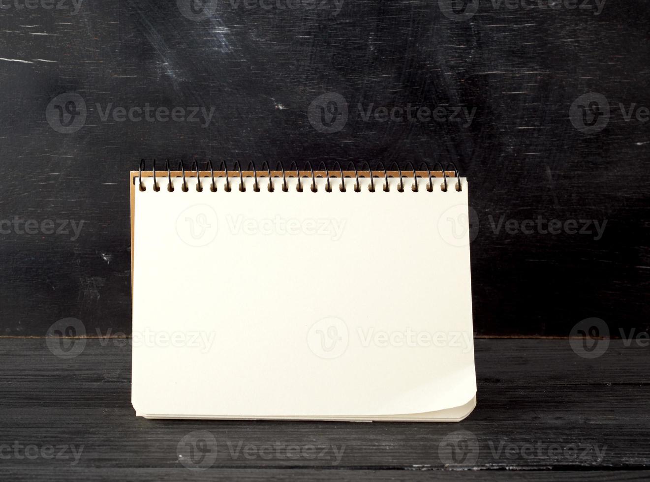 open spiral notebook with blank white sheets against a black chalk board photo