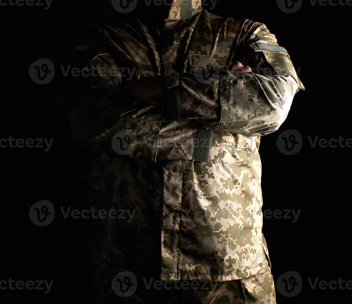 Ukrainian soldier in camouflage uniform stands with arms crossed on his chest photo