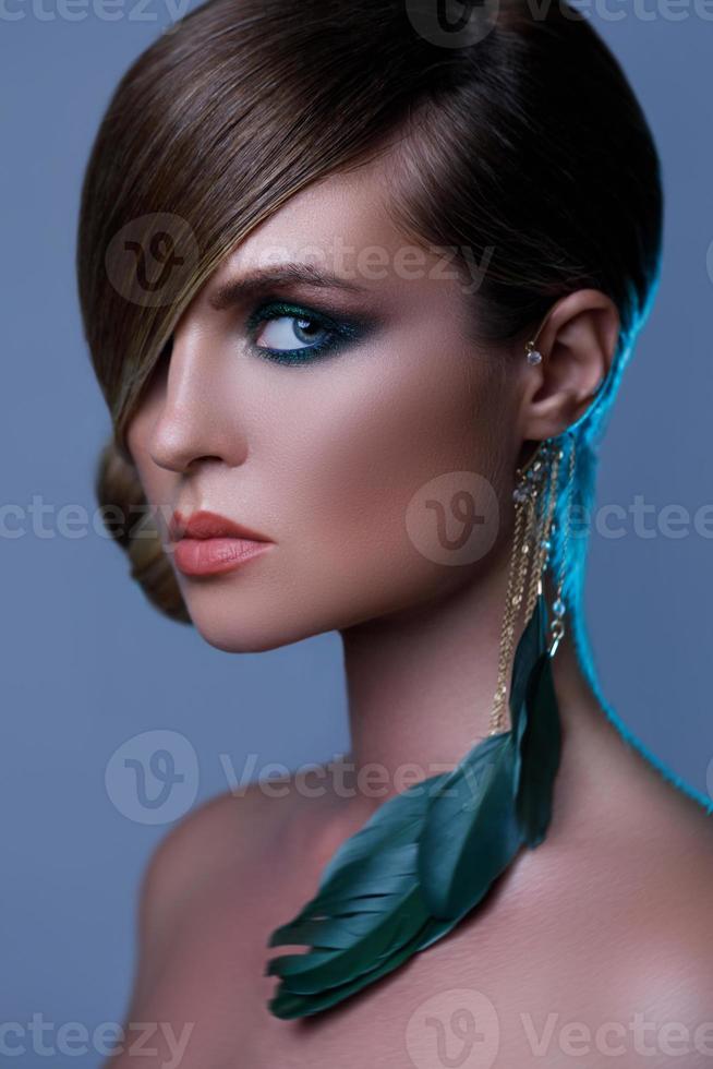 Model in stylish image with sleek hair covering one eye and feather earring photo