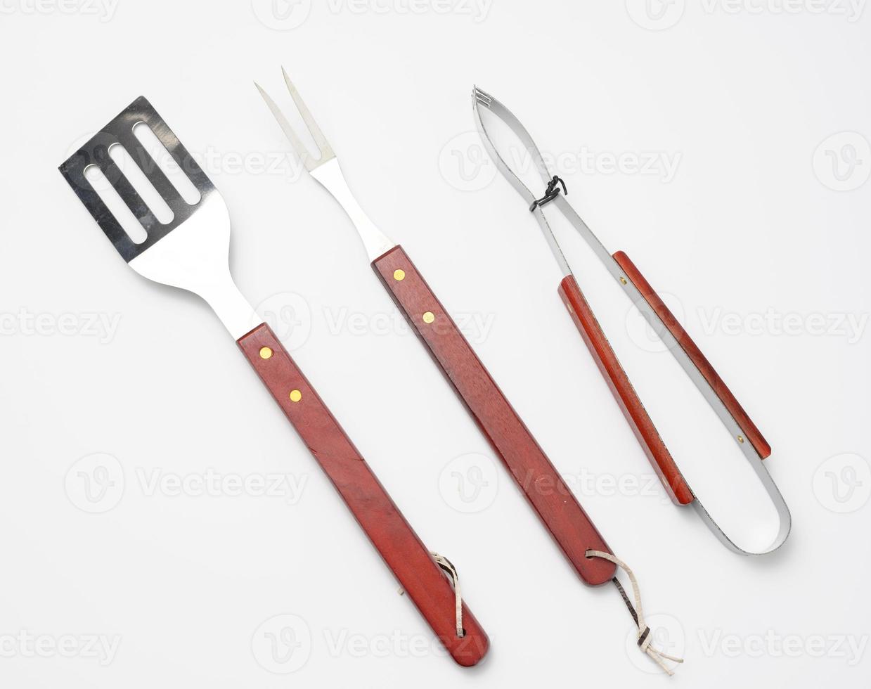 pinzas, espátula de metal y un tenedor con mango de madera sobre un fondo blanco foto