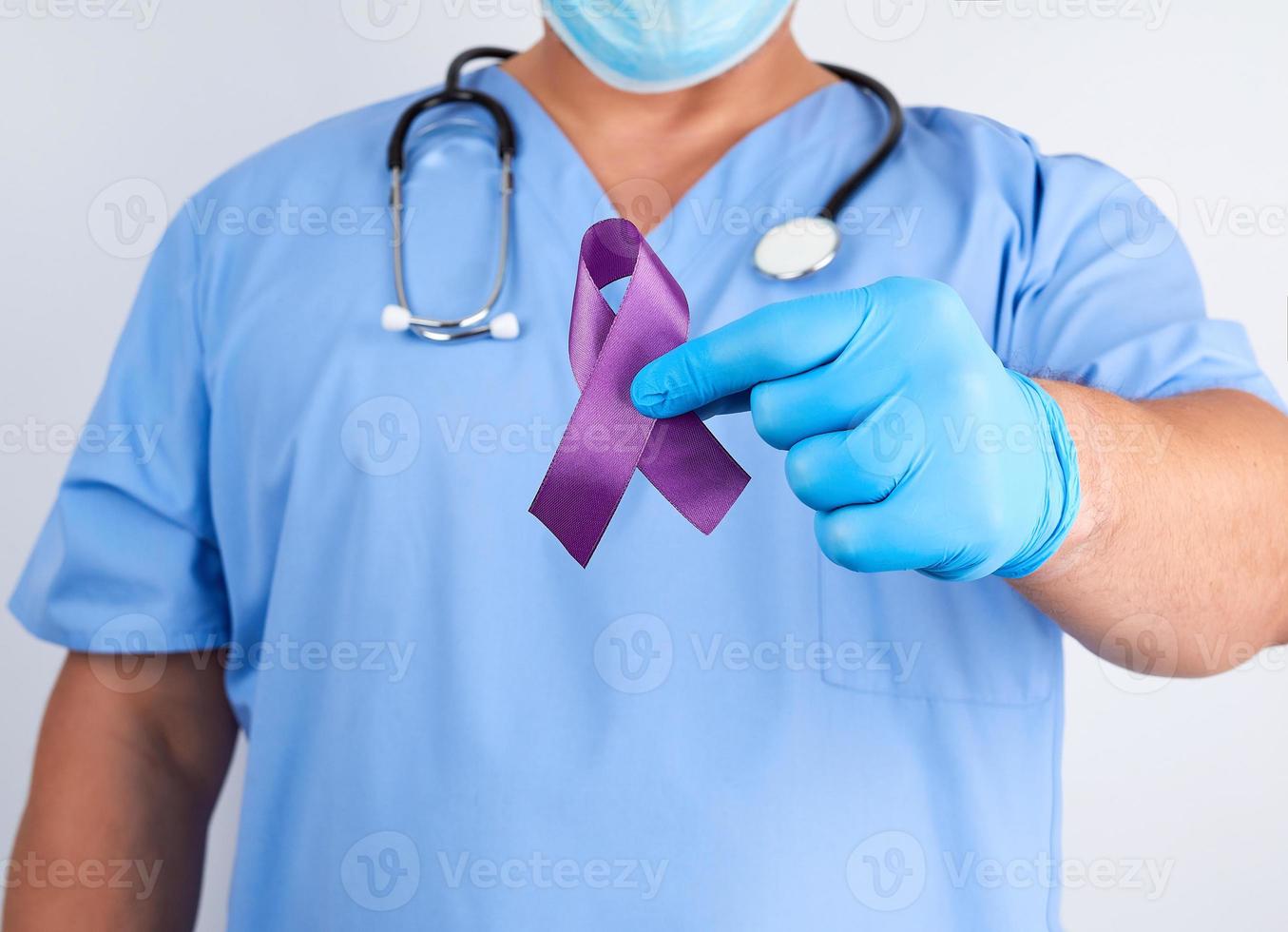 doctor in blue uniform and latex gloves holds a purple ribbon as a symbol of early research and disease control photo